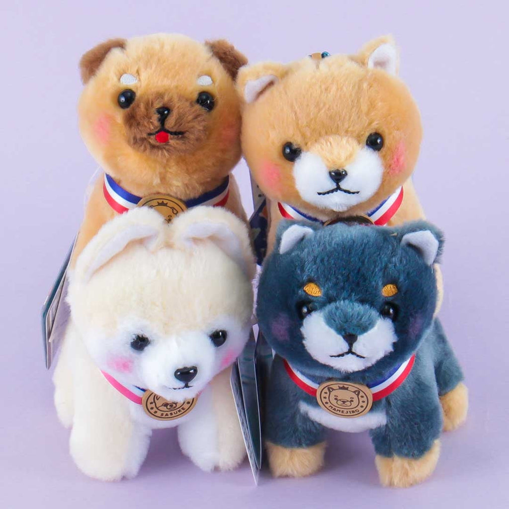 Three plushie charms in the shape of stylized dogs, each with a different color—one is beige, one is white, and one is gray—and each wearing a gold, silver, and bronze medal respectively.